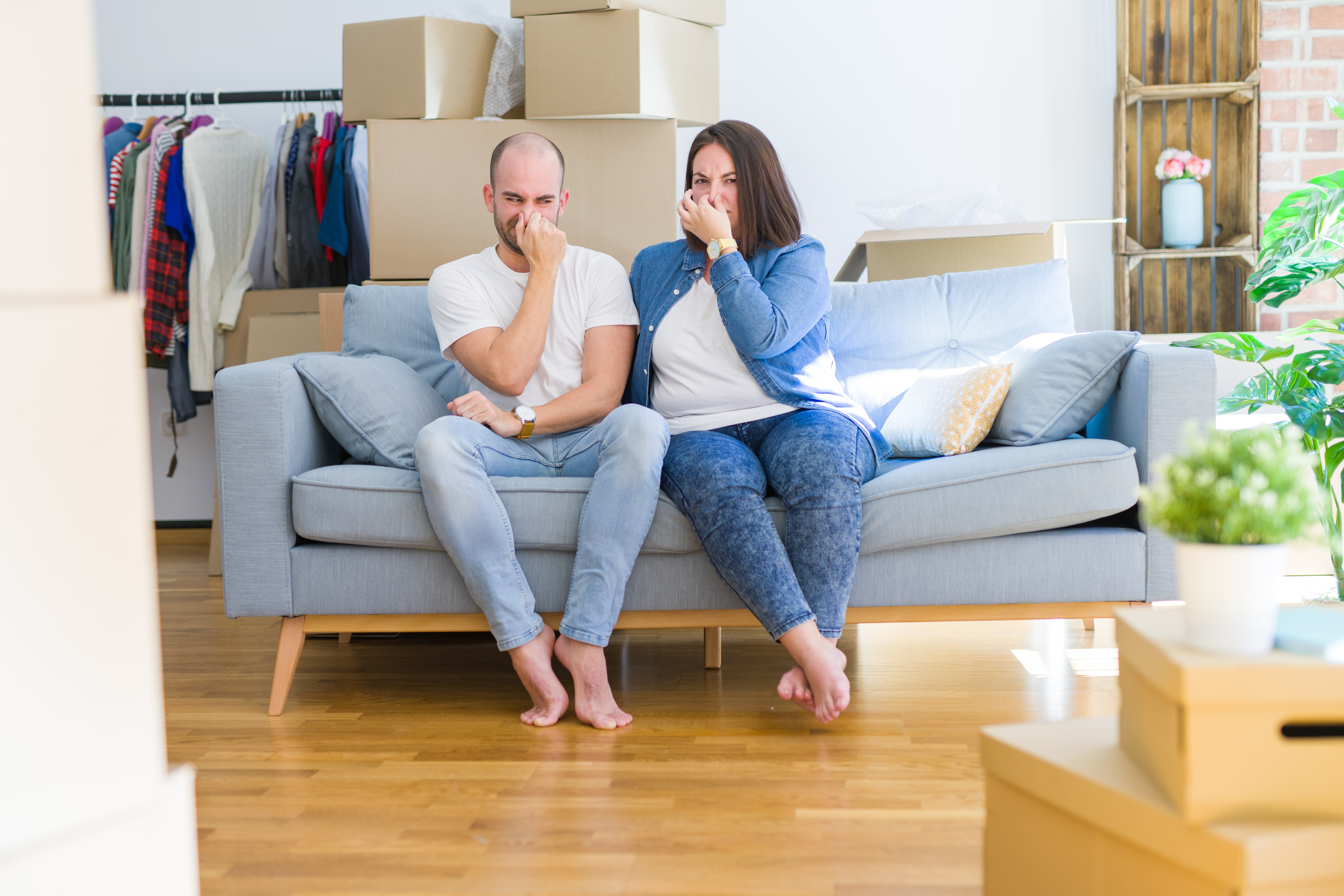 Young couple sitting on the sofa around cardboard boxes smelling something stinky