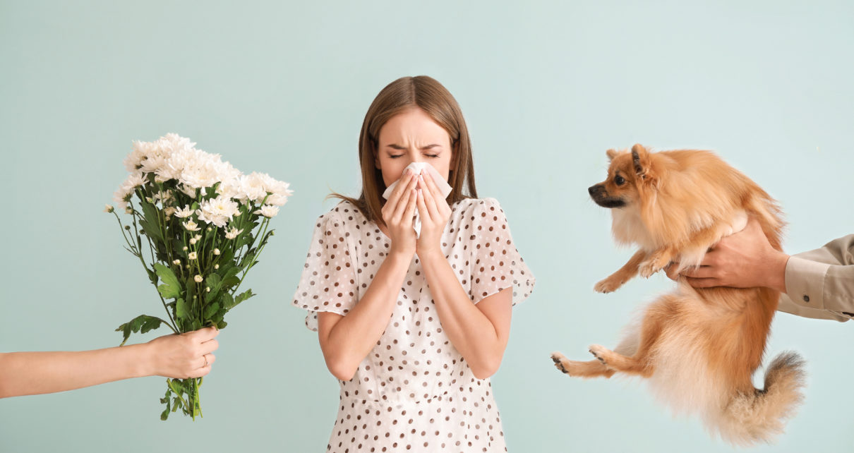 People giving flowers and dog to young woman blowing her nose from allergies