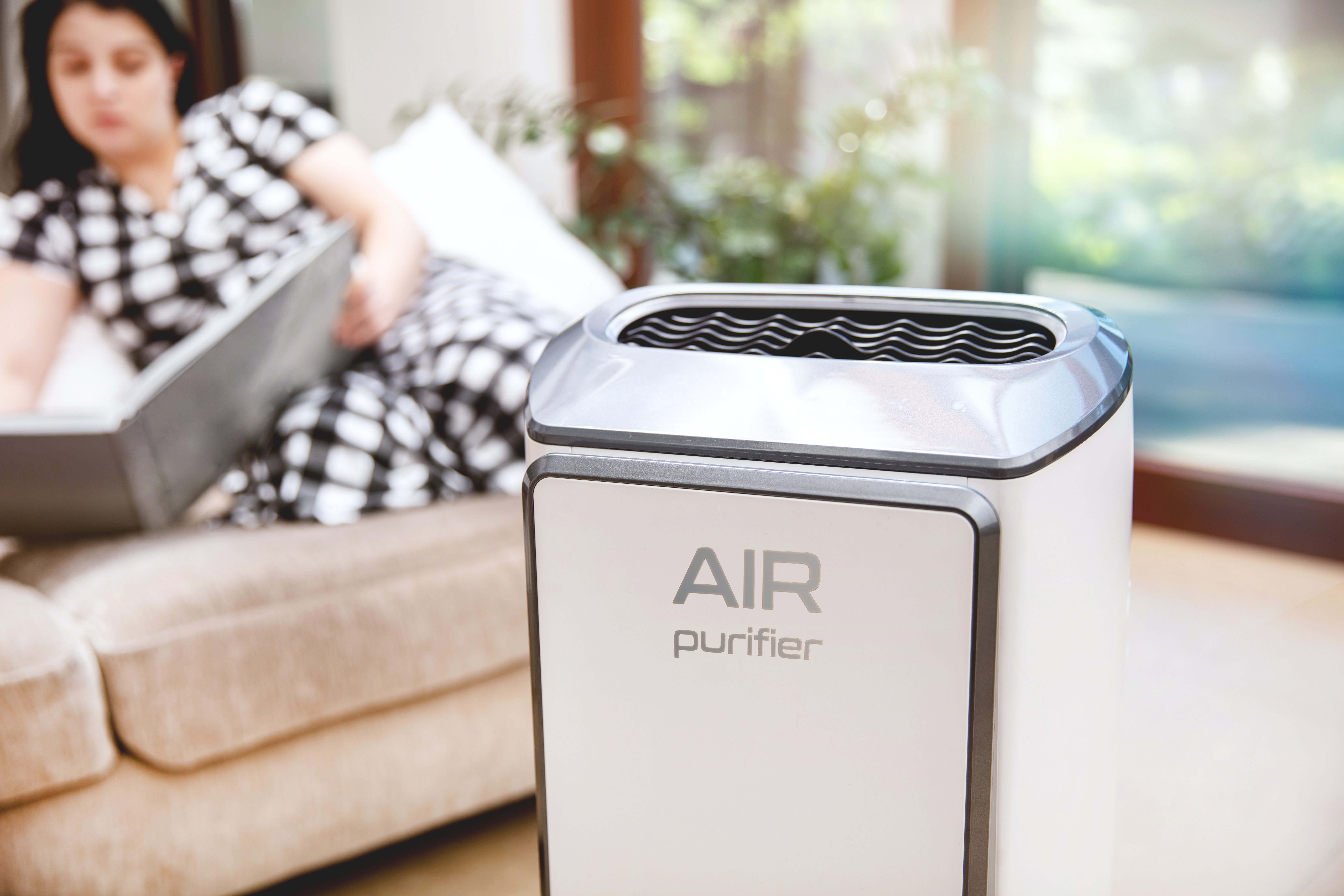 Woman reading book on couch of of focus with air purifier nearby [benefits of air purifier]