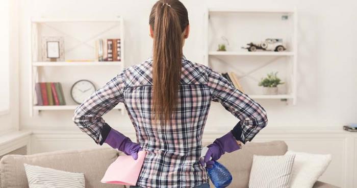 woman with hands on hips holding cleaning supplies in living room