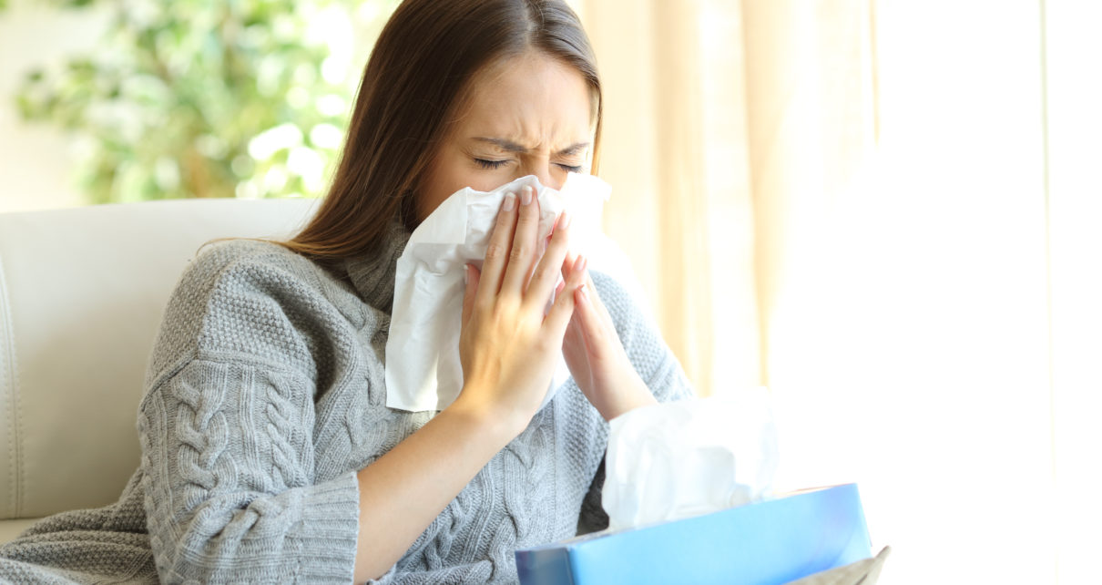 woman blowing nose next to box of tissues