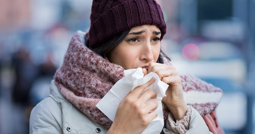 woman outside in winter clothes coughing into hands with tissue