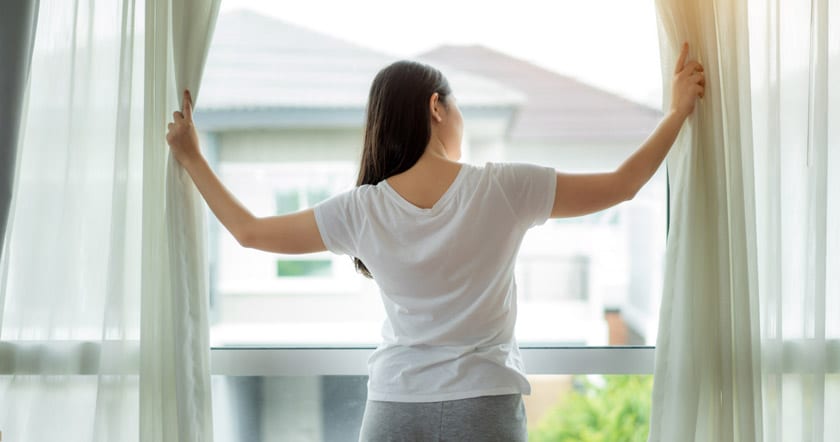 woman standing in window holding curtains open admiring outside
