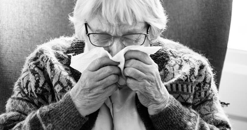 Elderly woman sneezing into tissue (black and white image)