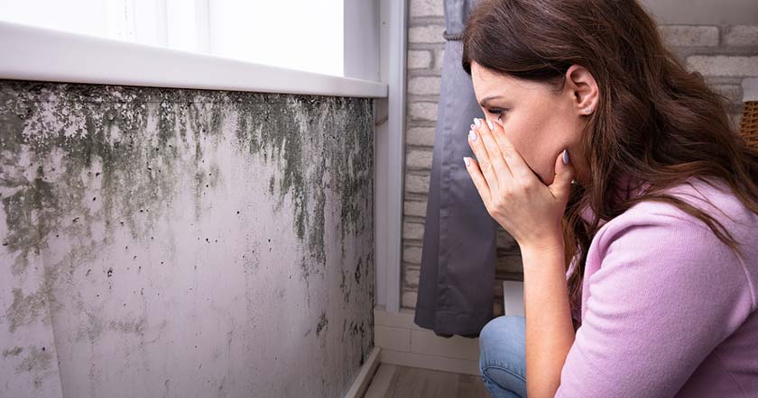 woman looking at black mold on walls holding breath