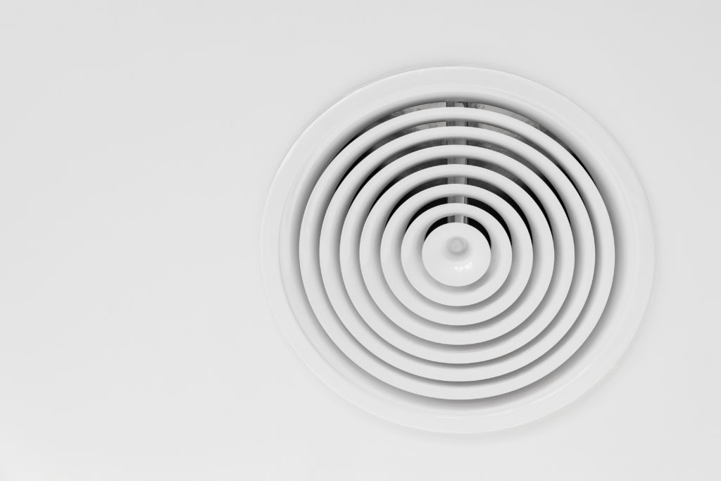 Round ventilation diffuser mounted in white ceiling, close-up photo