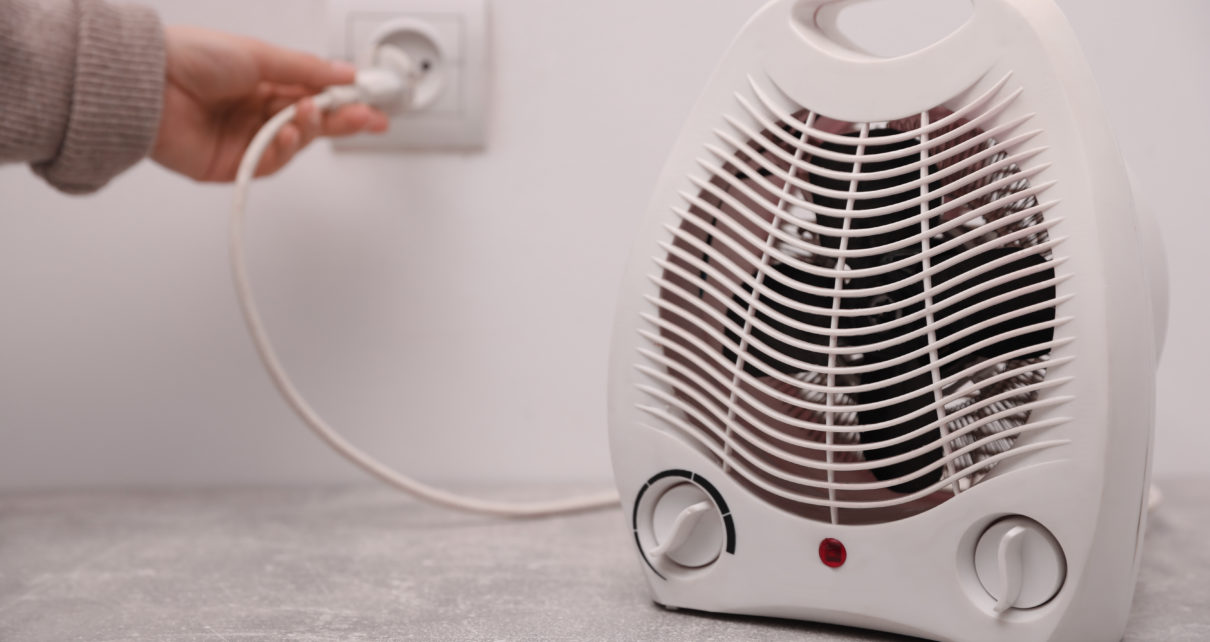 Woman plug in modern electric space heater indoors