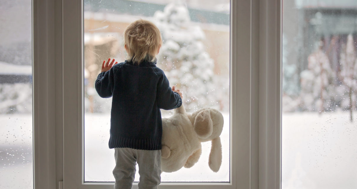 Toddler child standing in front of a big french doors overlooking snowy weather outside