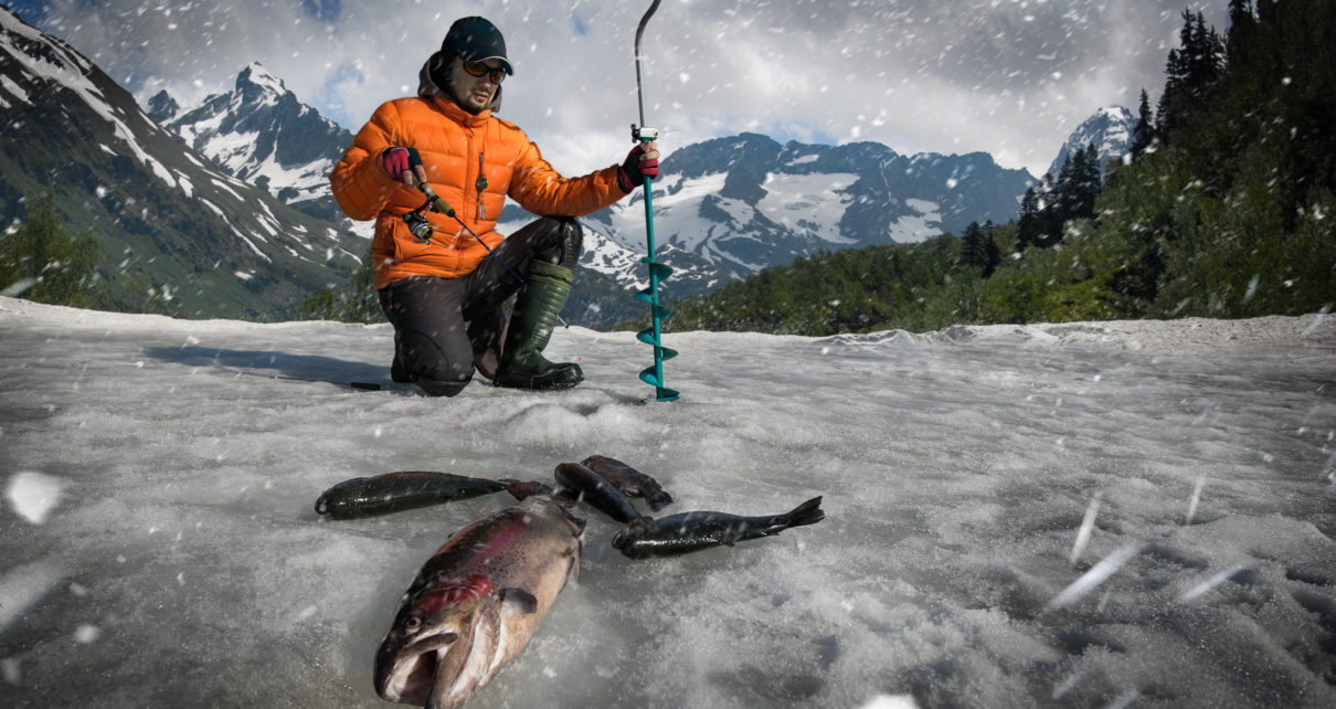 man ice fishing with several fish on ice