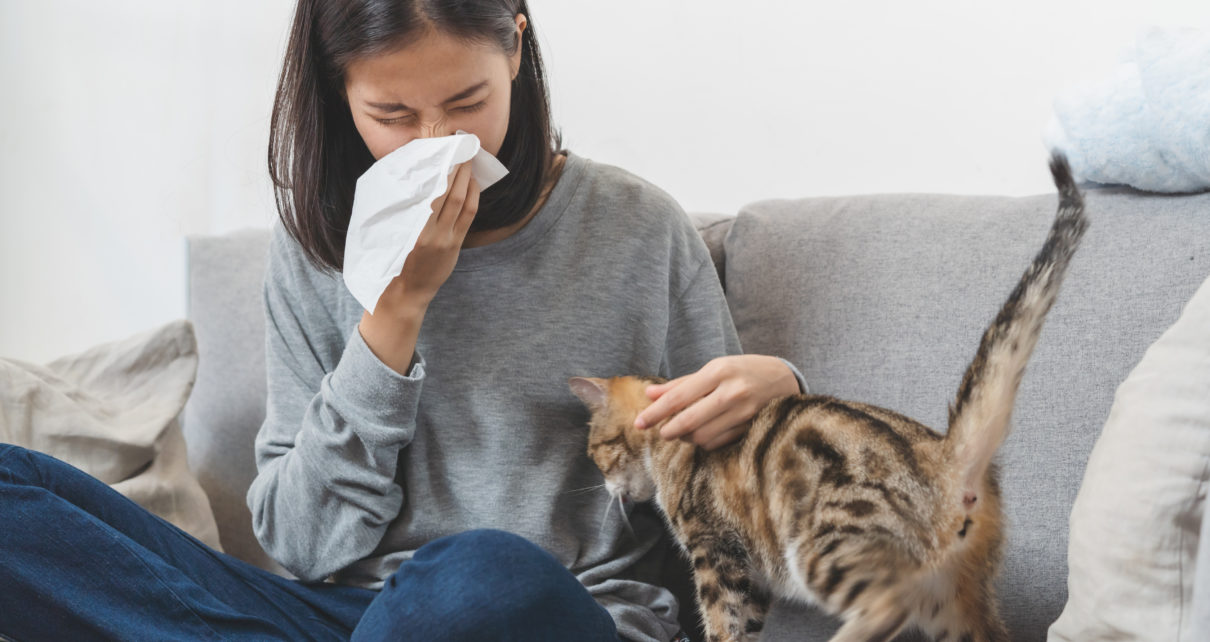 woman blowing her nose with cat next to her