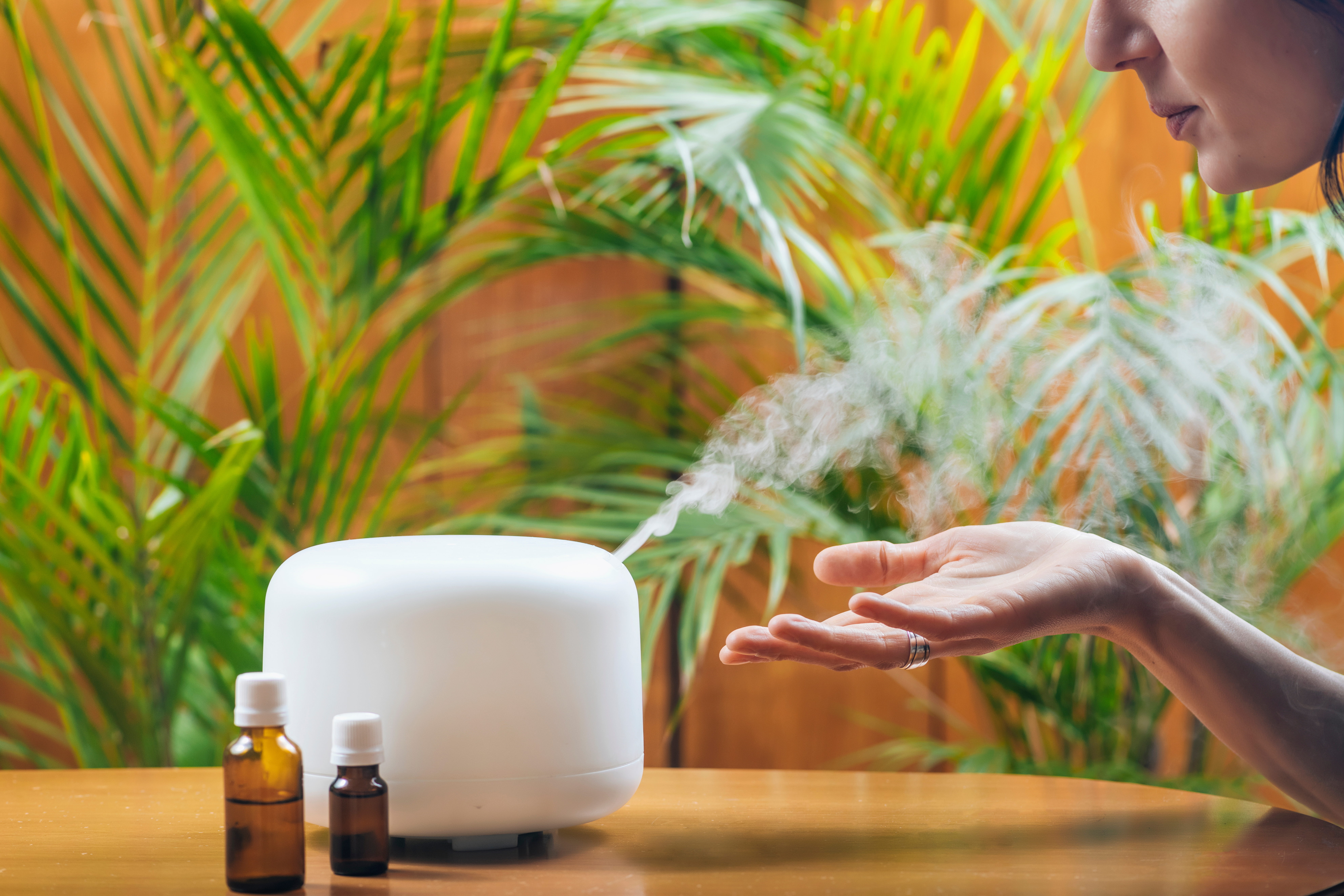 woman holding hand out in front of essential oil humidifier with two bottles of essential oil in forefront